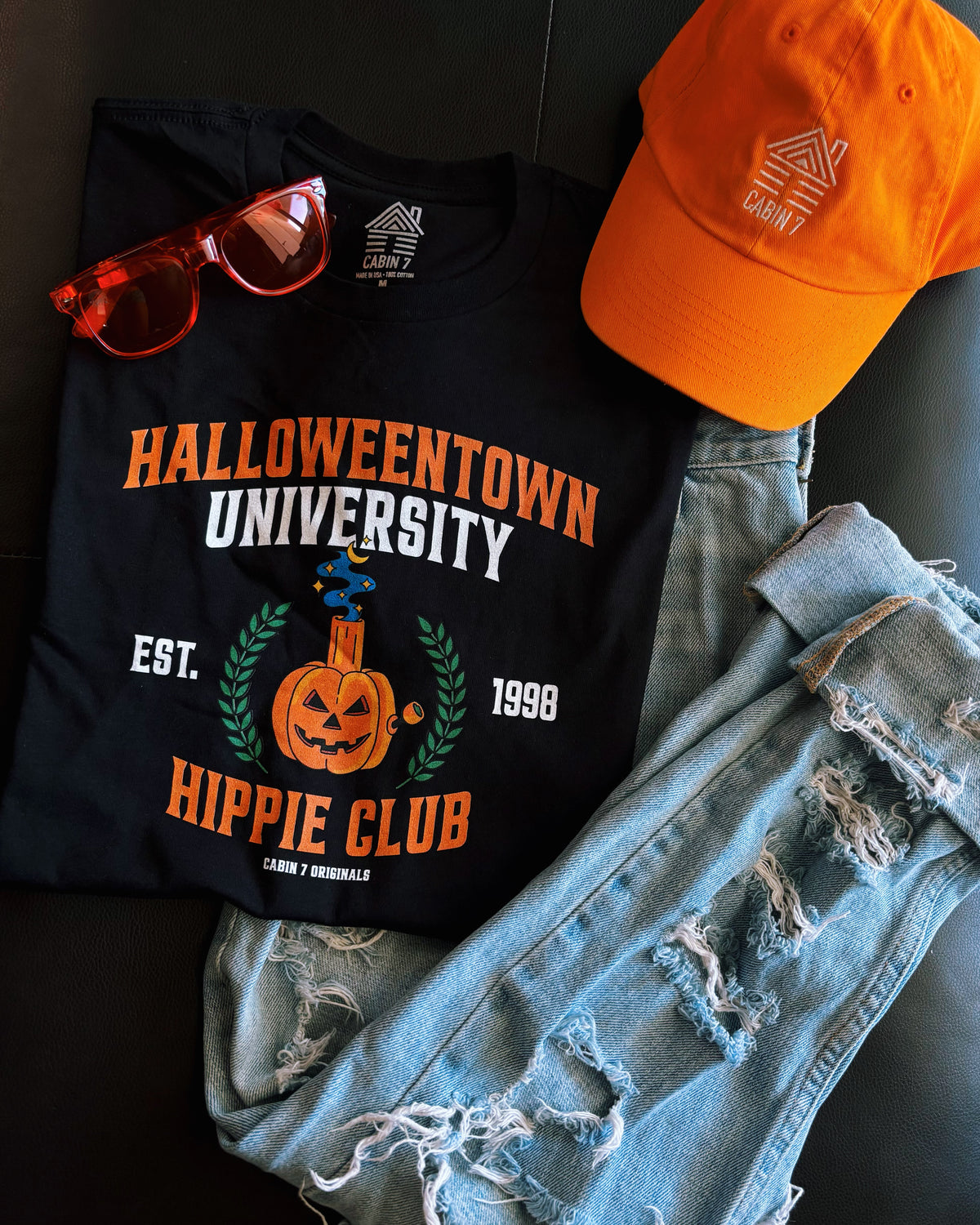 A black t-shirt with a stoner Halloween themed design that reads "Halloweentown University Hippie Club" and a pumpkin bong. Stoner shirts, Halloween apparel.