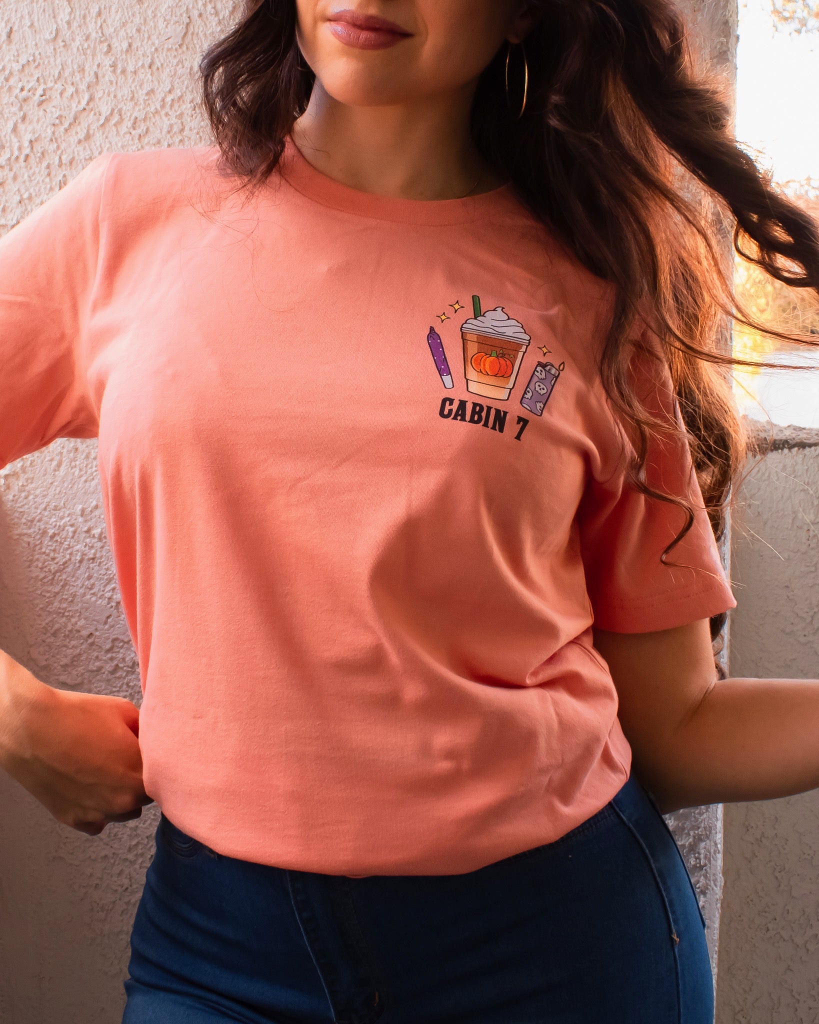 An orange t-shirt with a bright colorful stoner design, featuring several items such as a lighter, a joint, and a pumpkin spice latte.