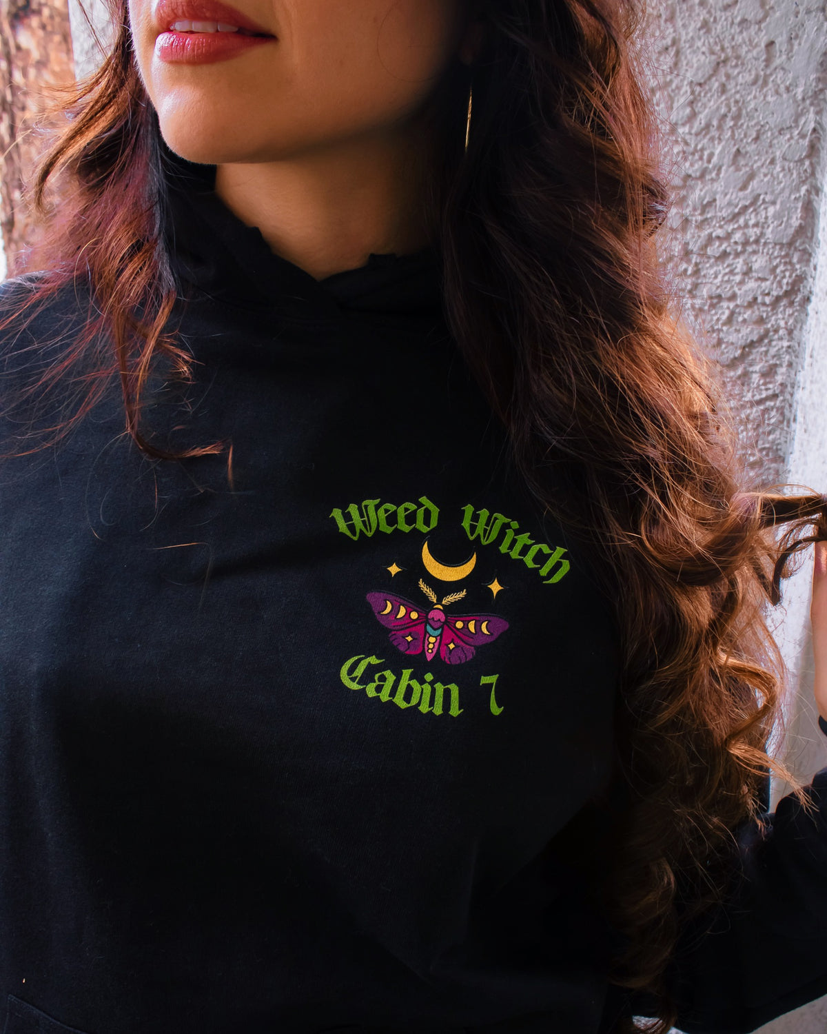 A black hoodie with a "Weed Witch" design, featuring a moth and a moon.