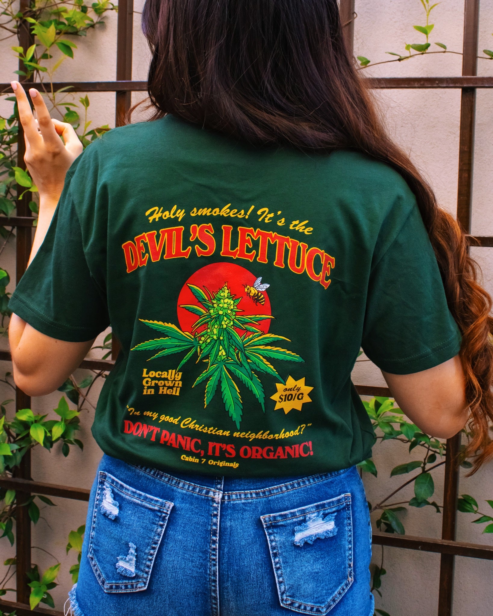 Person wearing back of green Cabin 7 cotton t-shirt with 'Devil's Lettuce, Don’t Panic, It’s Organic’ graphic.