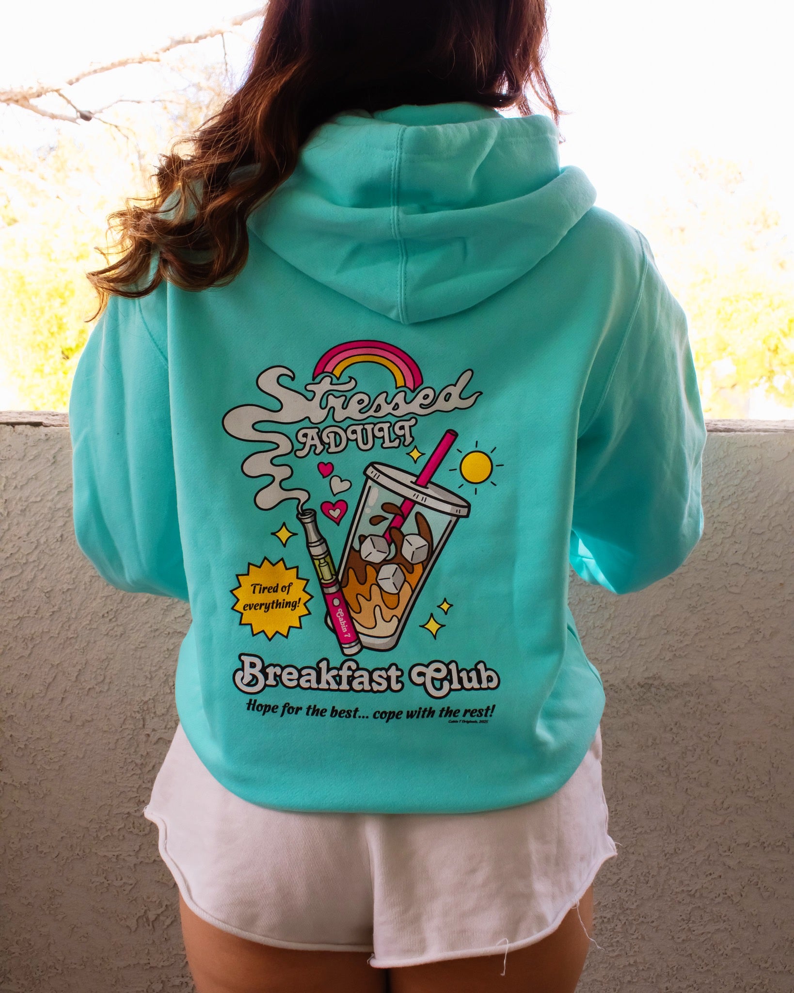 A mint-turquoise hoodie with a brightly colored design with an iced coffee and a cannabis vape pen, reading "Stressed Adult Breakfast Club". Hippie hoodie, 420 hoodie, stoner apparel.