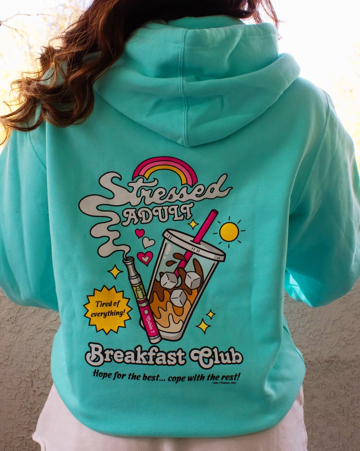 A mint-turquoise hoodie with a brightly colored design with an iced coffee and a cannabis vape pen, reading "Stressed Adult Breakfast Club". Hippie hoodie, 420 hoodie, stoner apparel.