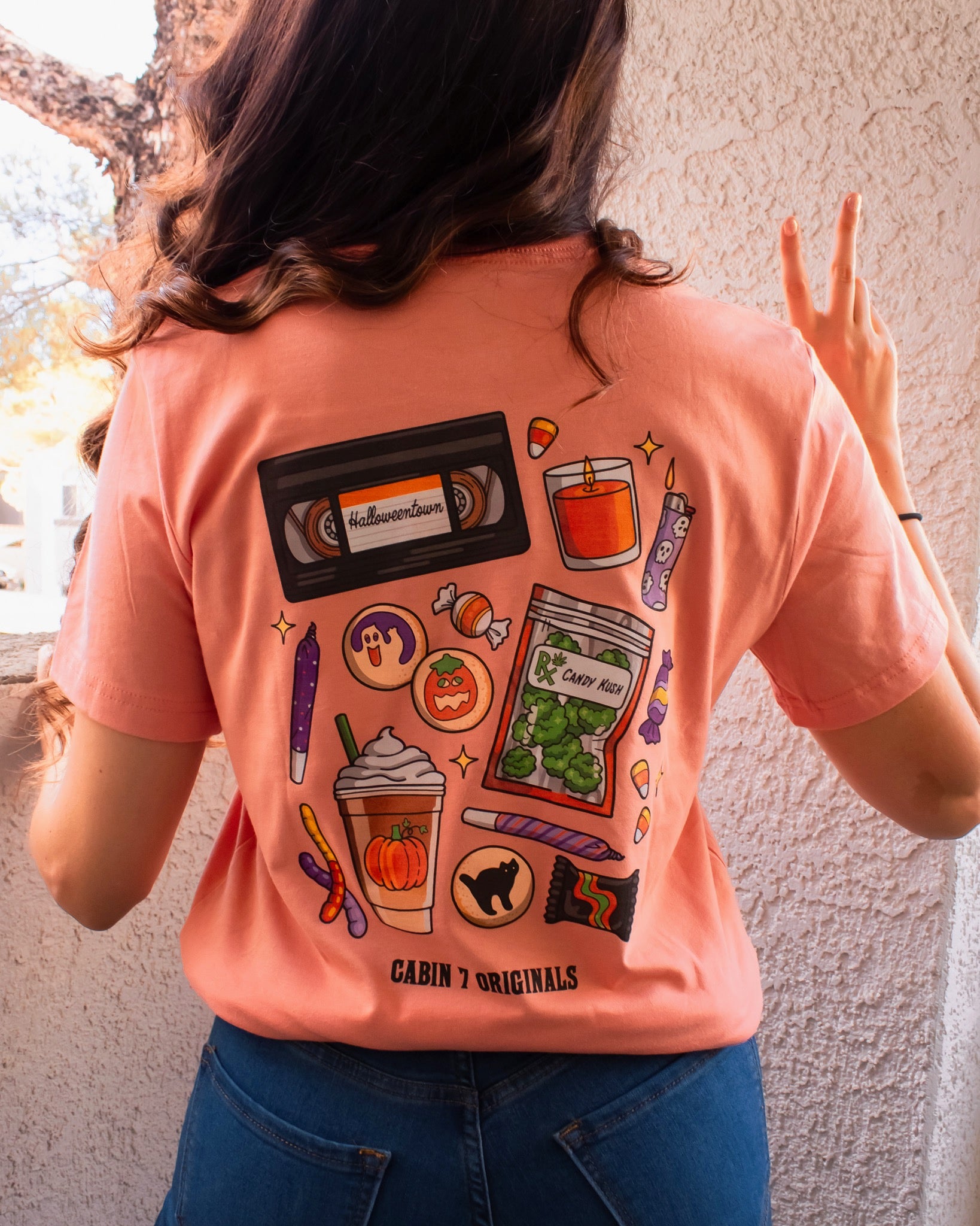 An orange t-shirt with a bright colorful stoner design, featuring several items such as a candle, a lighter, a VHS tape, and a bag of cannabis. 