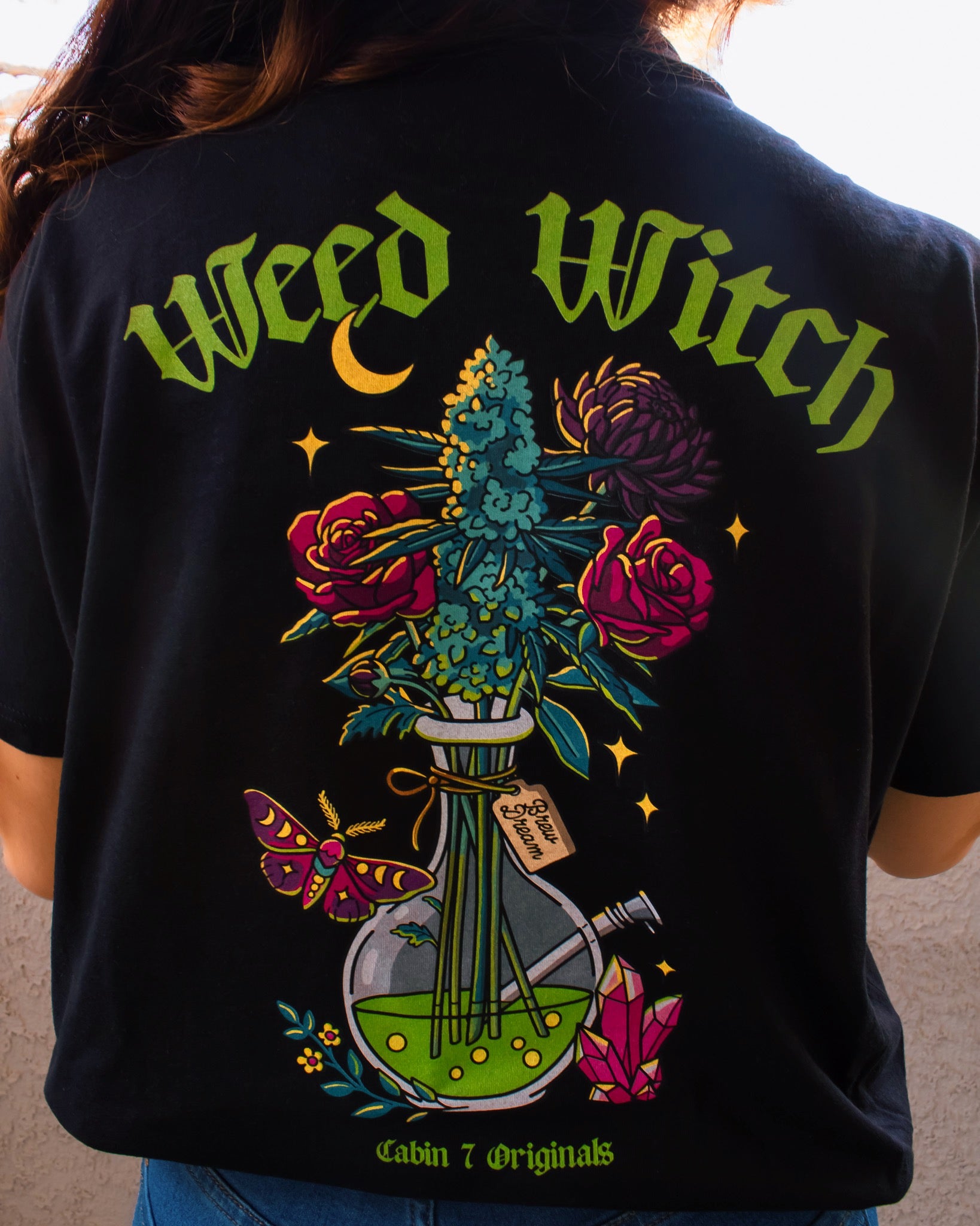 A black t-shirt with lime green text reading "Weed Witch" and a bong full of flowers and cannabis. Stoner witch apparel, spooky stoner apparel, hippie Halloween apparel.