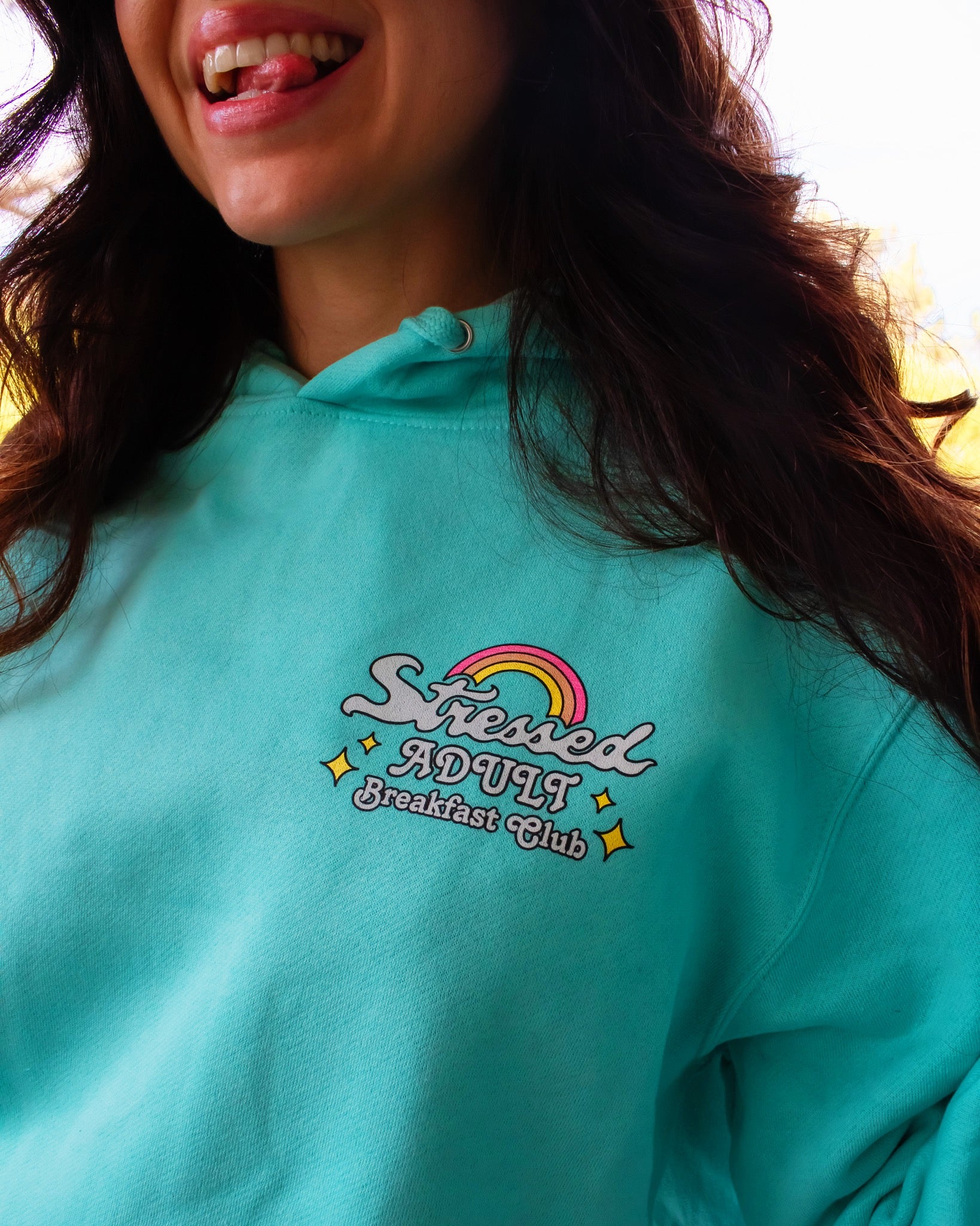 A mint-turquoise hoodie with a brightly colored design reading "Stressed Adult Breakfast Club". Hippie hoodie, 420 hoodie, stoner apparel.