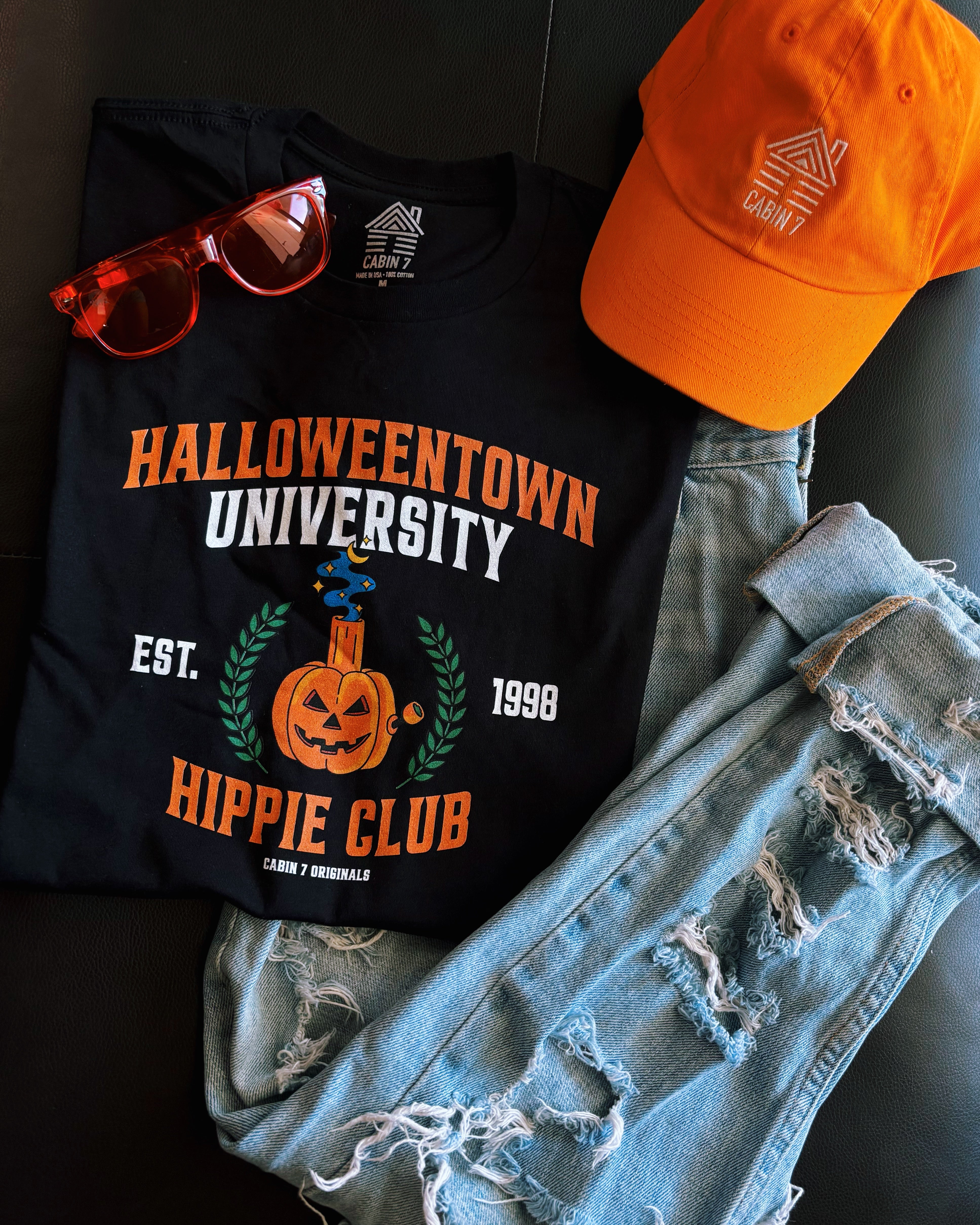 A black t-shirt with a stoner Halloween themed design that reads "Halloweentown University Hippie Club" and a pumpkin bong. Stoner shirts, Halloween apparel.