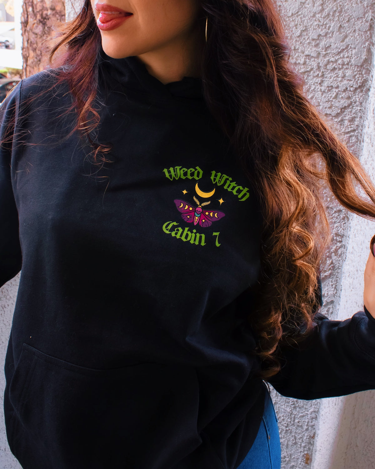 A black hoodie with a "Weed Witch" design, featuring a moon and a moth.