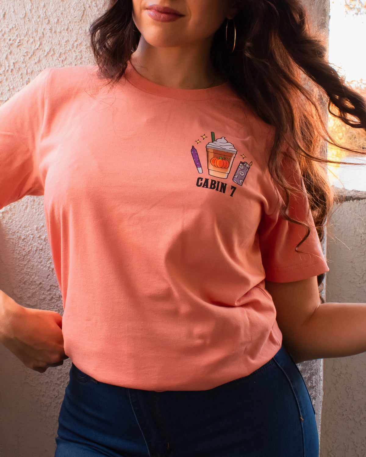 An orange t-shirt with a bright colorful stoner design, featuring several items such as a lighter, a joint, and a pumpkin spice latte.