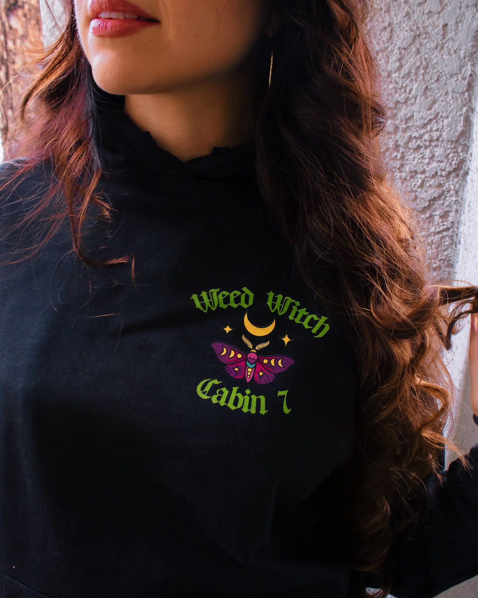 A black hoodie with a "Weed Witch" design, featuring a moth and a moon.