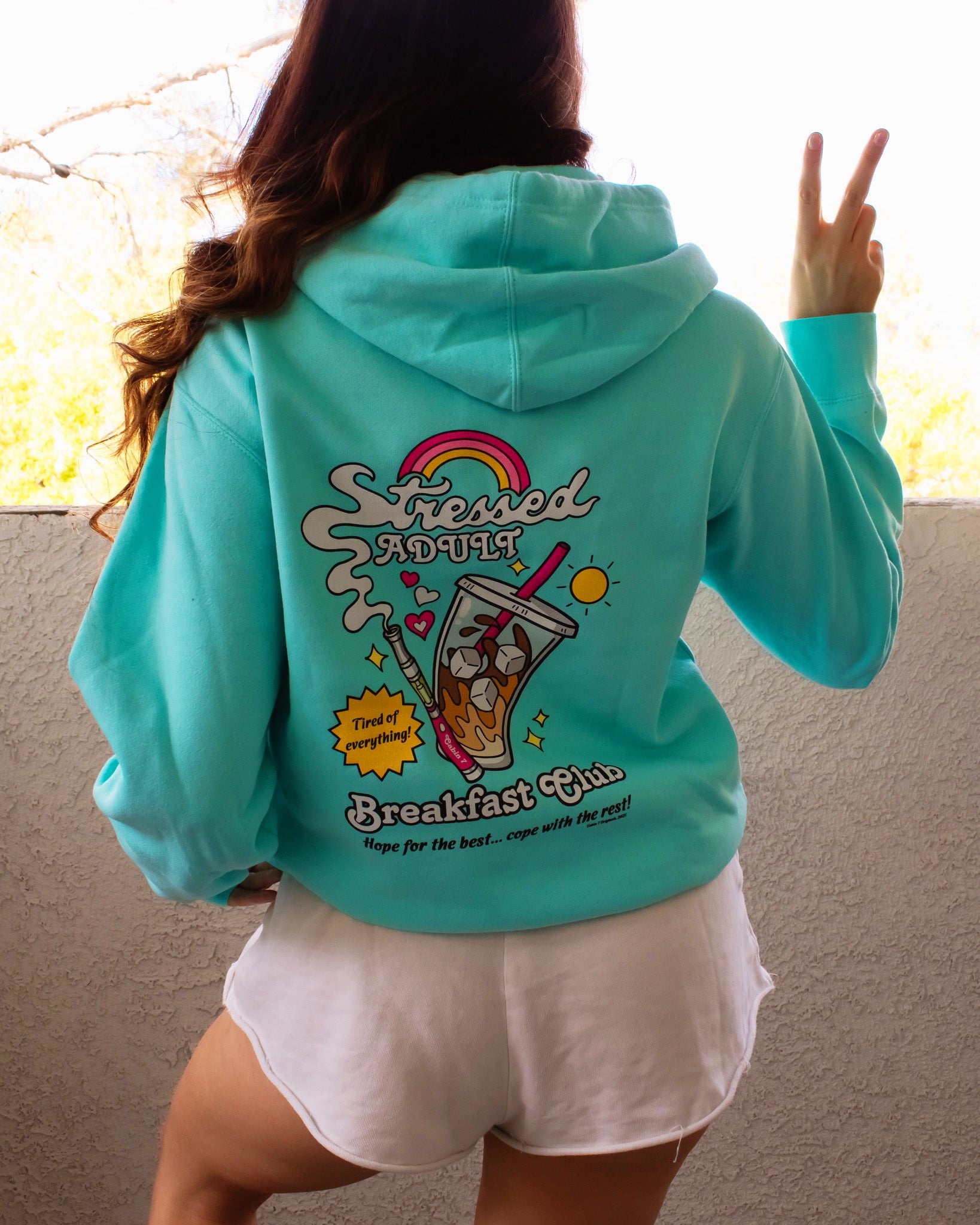 A mint-turquoise hoodie with a brightly colored design with an iced coffee and a cannabis vape pen, reading "Stressed Adult Breakfast Club". Hippie hoodie, 420 hoodie, stoner apparel.