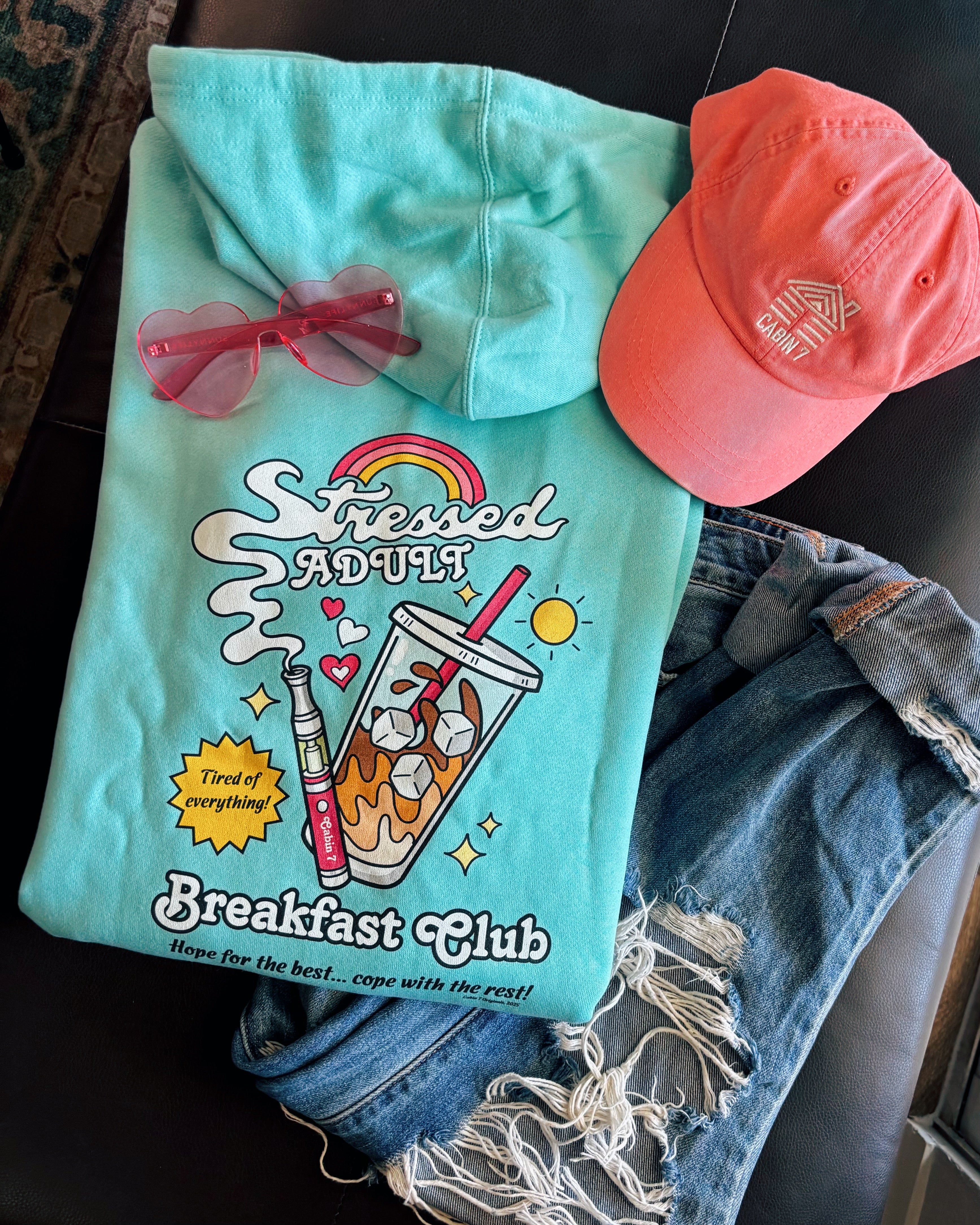 A mint-turquoise hoodie with a brightly colored design with an iced coffee and a cannabis vape pen, reading "Stressed Adult Breakfast Club". Hippie hoodie, 420 hoodie, stoner apparel.