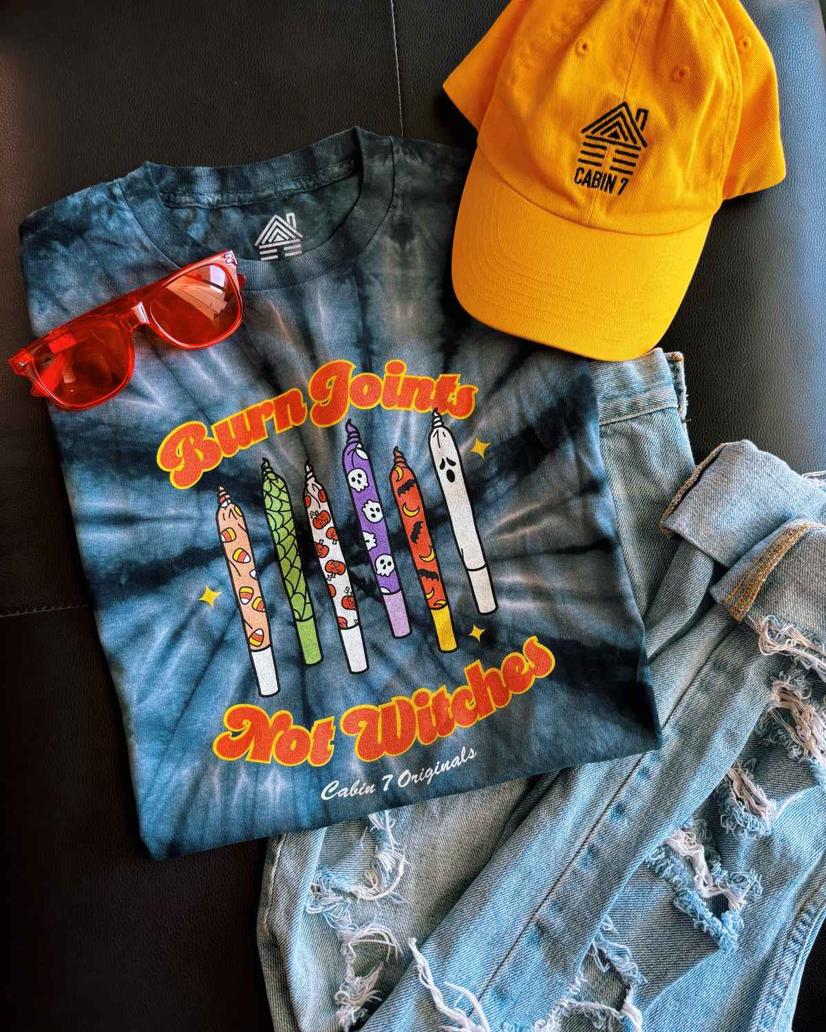 Black tie-dye shirt with colorful halloween design on front, featuring multiple spooky joints and the text "Burn Joints Not Witches".