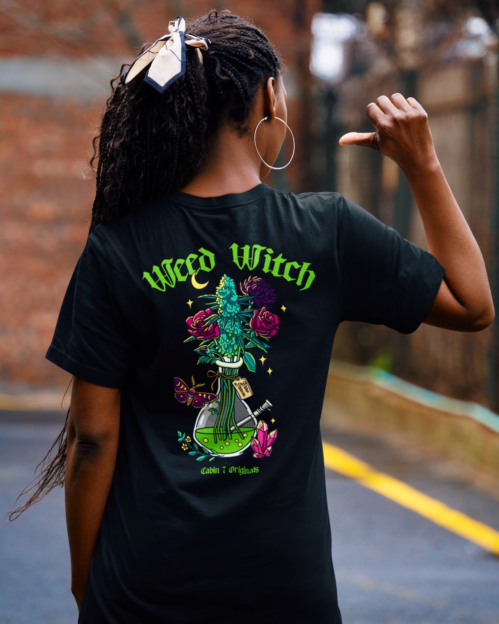 A black t-shirt with lime green text reading "Weed Witch" and a bong full of flowers and cannabis. Stoner witch apparel, spooky stoner apparel, hippie Halloween apparel.