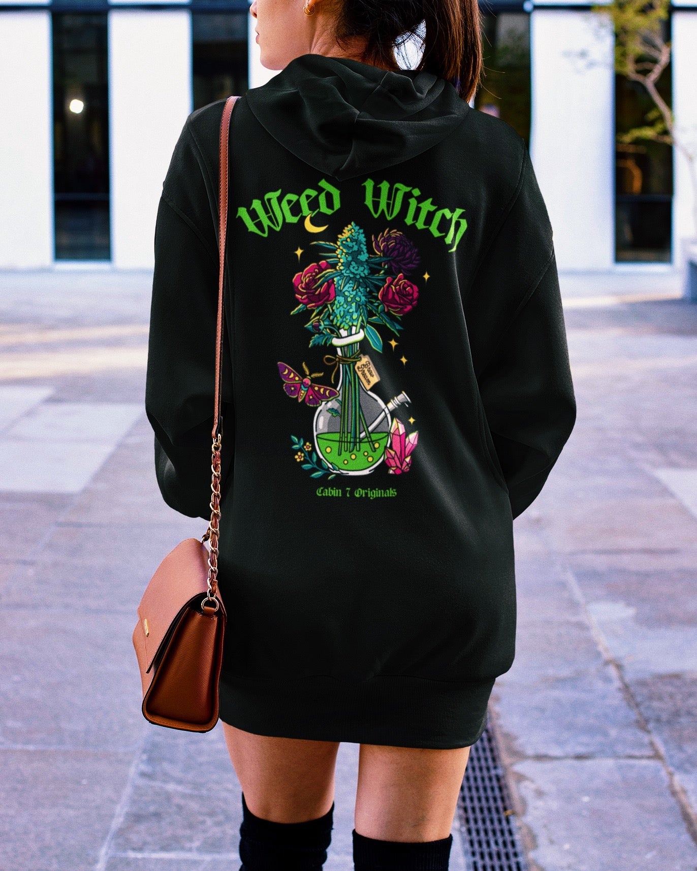A black hoodie with a "Weed Witch" design, featuring a bong filled with flowers and a cannabis plant, as well as a moth, a moon, and crystals. Weed witch apparel, stoner Halloween
